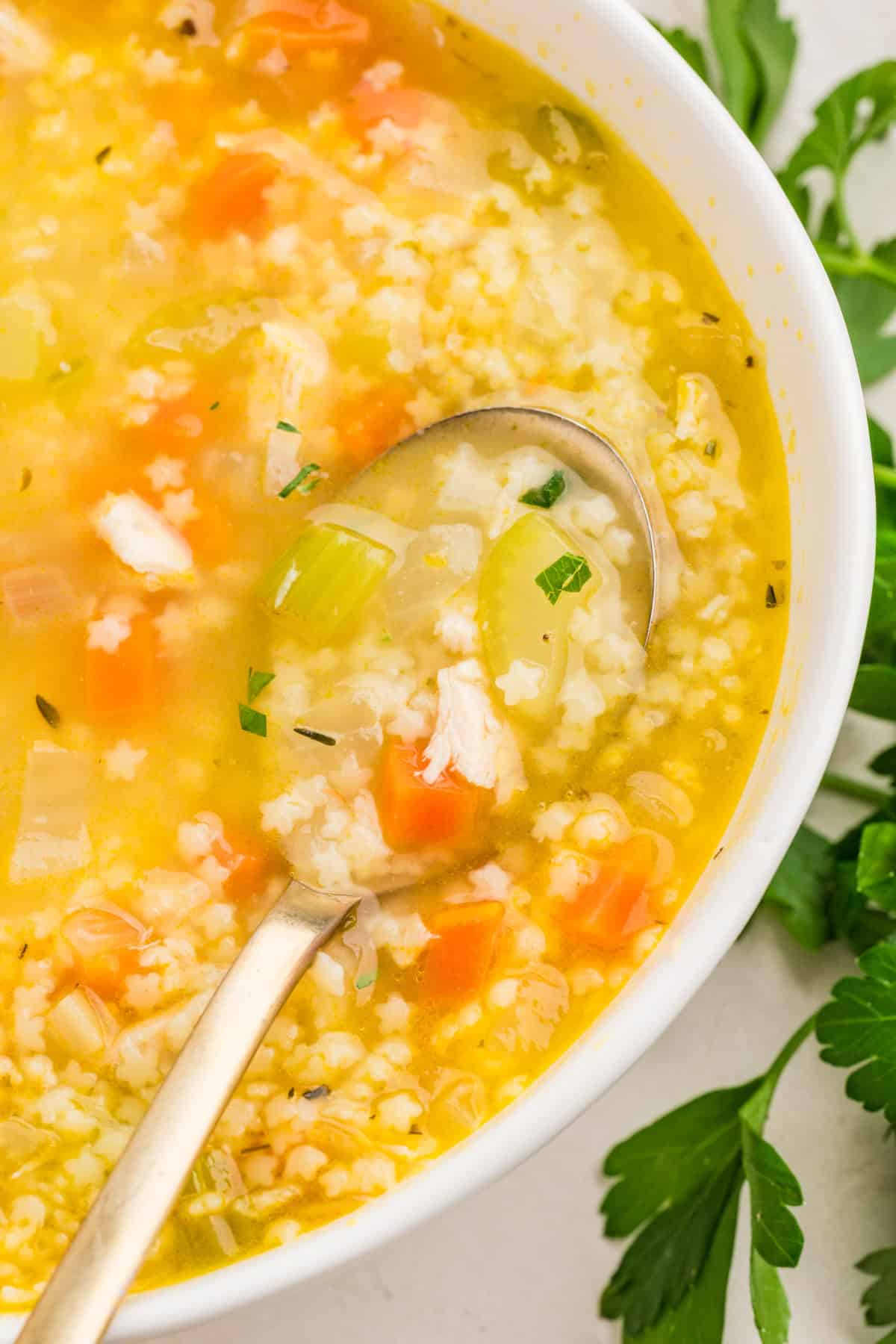 Overhead shot of chicken pastina soup in a white bowl with a spoon