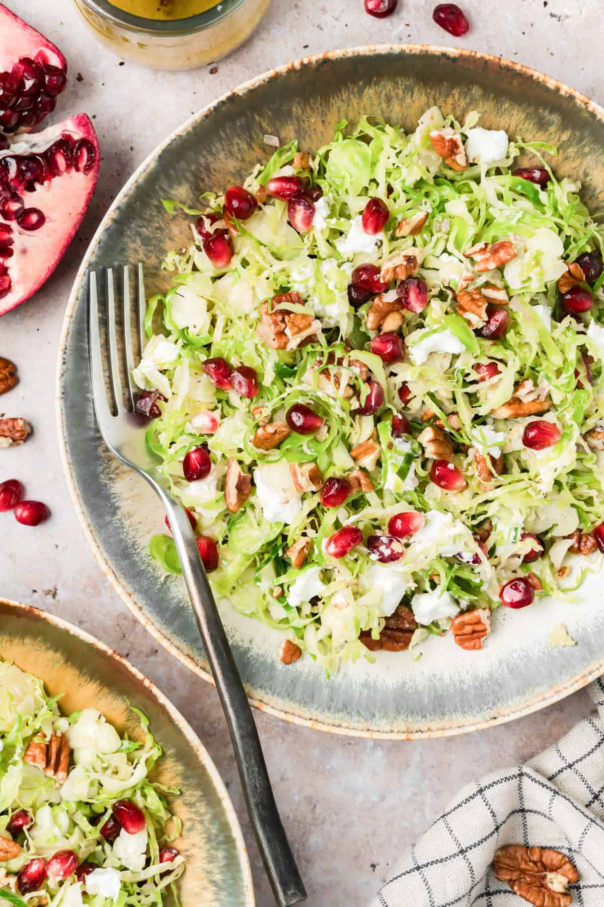 Shaved Brussels sprouts salad with pomegranate, pecans, and goat cheese on a table with scattered pomegranate arils