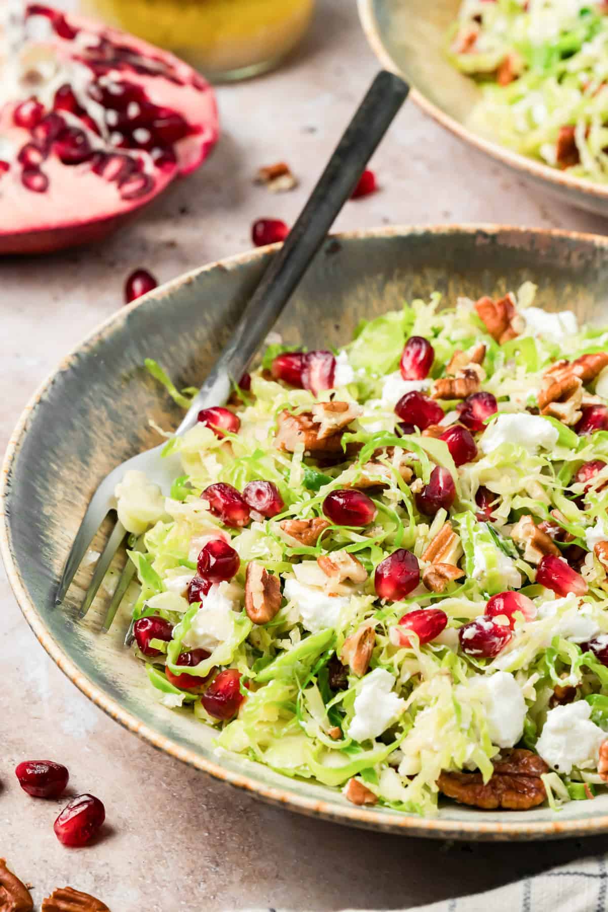 Shaved Brussels sprouts salad with pomegranate arils, pecans, and goat cheese in a serving bowl
