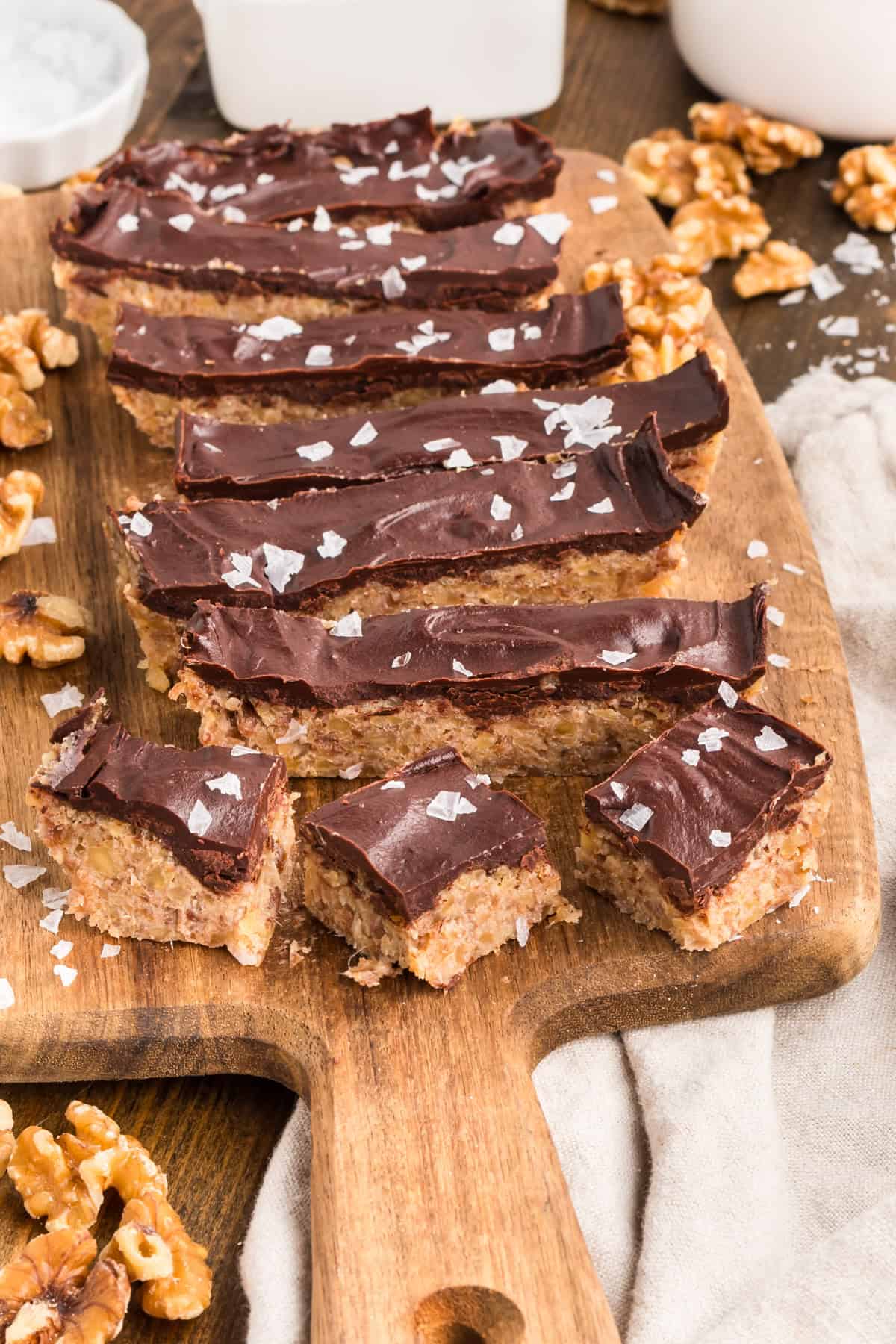 Chocolate walnut date bars topped with flaky sea salt and cut into squares on a wooden board.